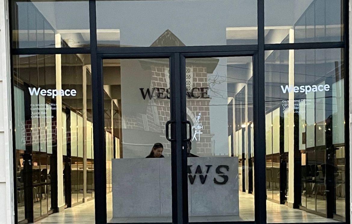 Entrance of Wespace co-working office with glass doors and interior view.