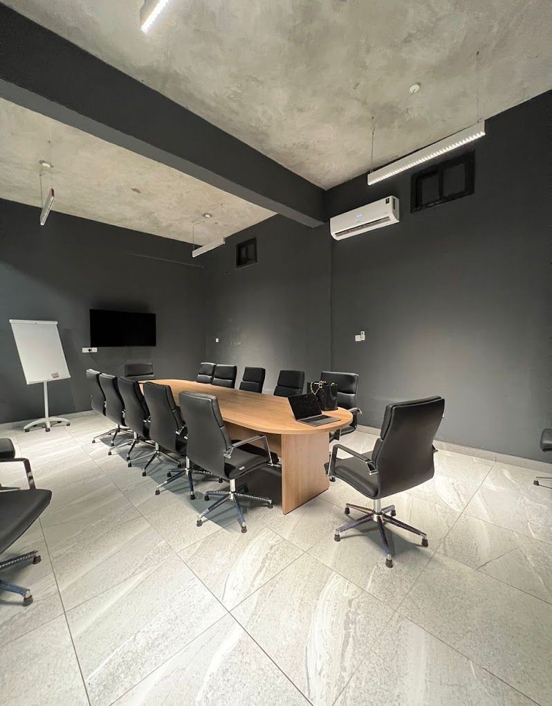 Modern conference room with a long wooden table, black chairs, and a wall-mounted screen.